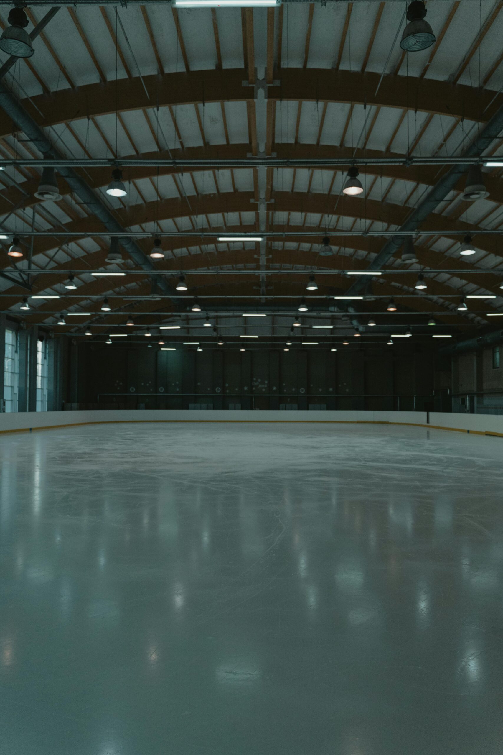 Spacious indoor ice skating rink with overhead industrial lighting.